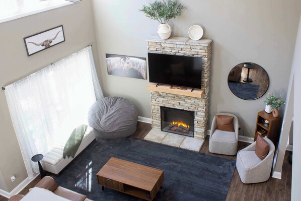Una sala de estar con chimenea de piedra, televisor de pantalla plana, sofá, sillón de peluche y una mesita de centro.