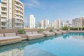 A rooftop pool with lounge chairs, a clear sky, and high-rise buildings in the background.