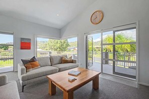 Ein modernes Wohnzimmer mit einer Couch, einem Couchtisch und großen Fenstern mit Blick auf Grünflächen und Gebäude.