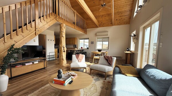 A spacious living area with a wooden staircase, a television, a sofa, and a dining table.