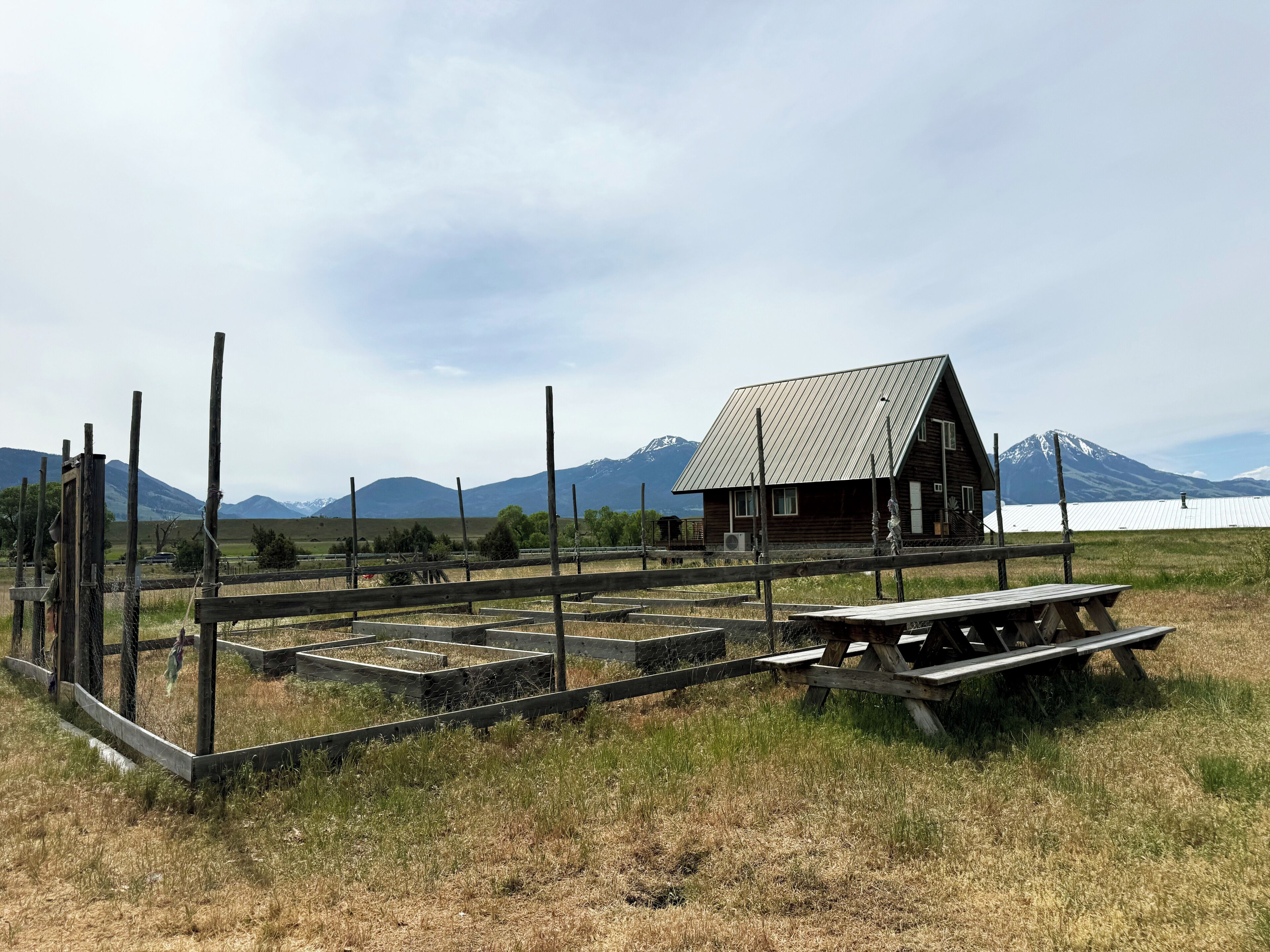 A rustic cabin with a metal roof, surrounded by a wooden fence and a picnic table.