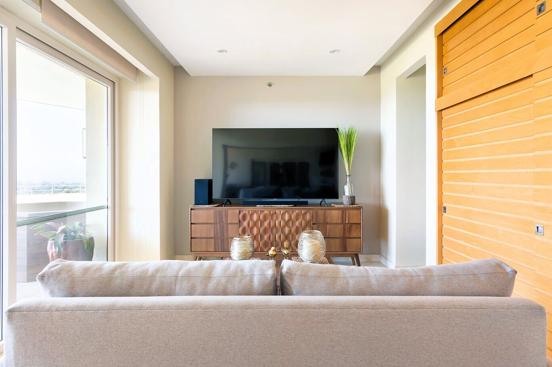 Un salón con sofá, televisor sobre un mueble de madera y vistas a través de un ventanal.