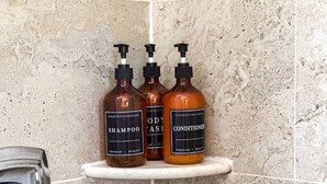 Three bottles of shampoo and conditioner on a white shelf in a bathroom with a speckled tile wall. - Salt Air Suites • king bed • Pool• Pets OK #2 (Clearwater)