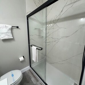 A modern bathroom with a glass shower enclosure, a toilet, and a towel rack.