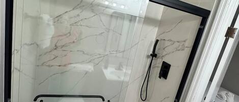Ducha con mampara de vidrio y marco negro, barandilla y cabezal de ducha.