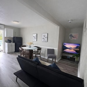 Ein modernes Wohnzimmer mit Sofa, Esstisch, Stühlen, einem Flachbildfernseher und Kunstwerken an den Wänden.