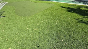 A backyard with artificial grass, a white fence, and trees. - Bright Coastal Stay • Pool • Near Beaches #3 (Clearwater)