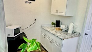 A compact kitchen with white cabinets, a microwave, and a small table with a plant. - Bright Coastal Stay • Pool • Near Beaches #3 (Clearwater)