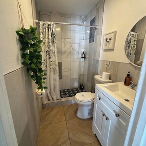 Een badkamer met douche, toilet, wastafel en spiegel.