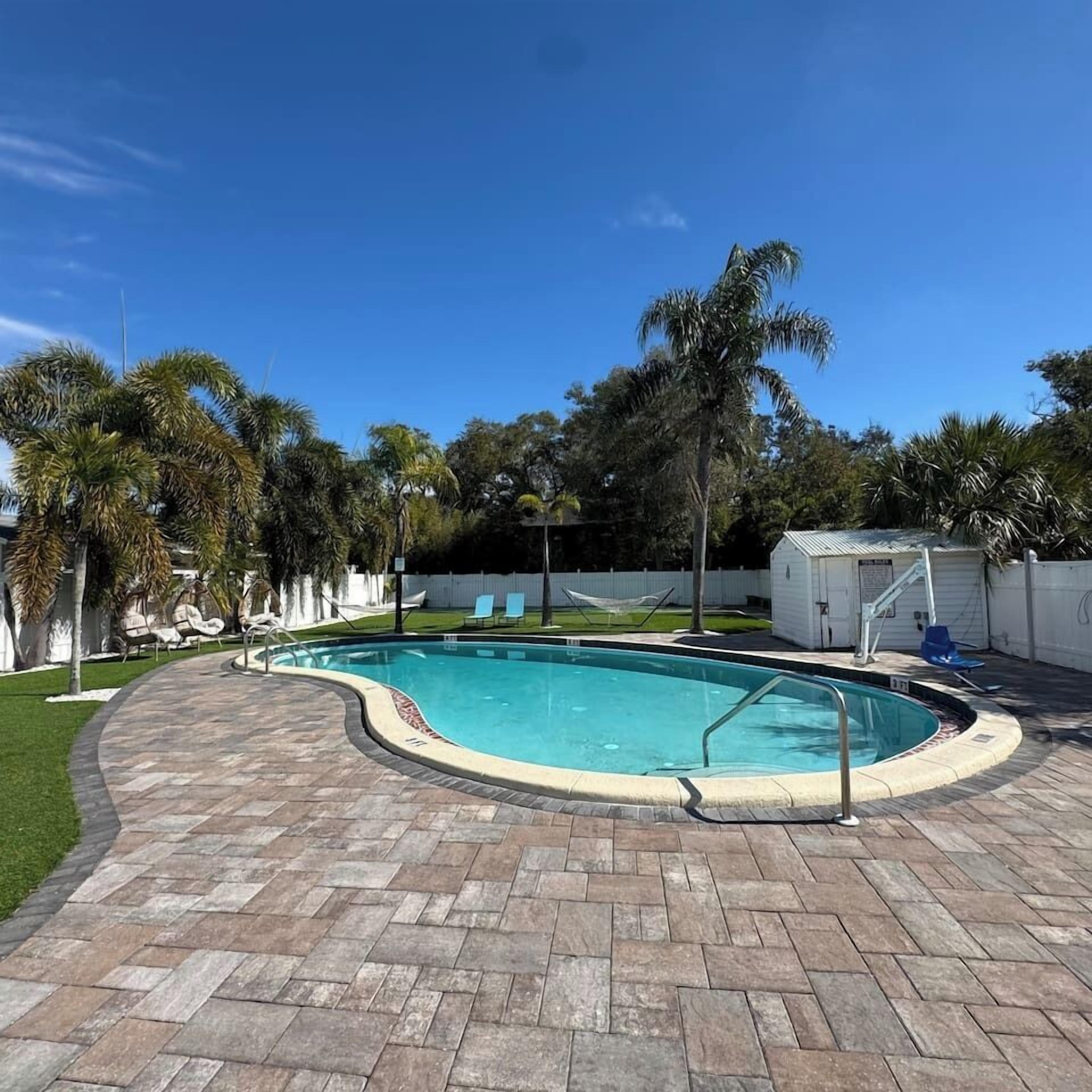 En pool med en böjd kant, omgiven av en stenlagd uteplats och palmer.