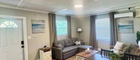 A living room with a sofa, a dining table with chairs, a lamp, and a small side table.