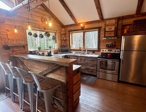 A rustic kitchen with wooden walls, a stainless steel refrigerator, a double oven, and a bar area with stools.
