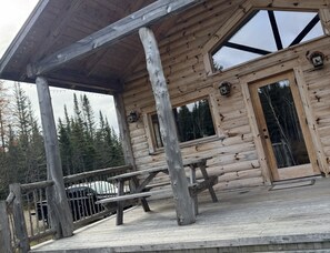 A wooden cabin with a covered porch, large windows, and a bench.