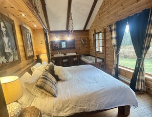 A wooden cabin bedroom with a bed, a mirror, a sink, and a window with curtains.