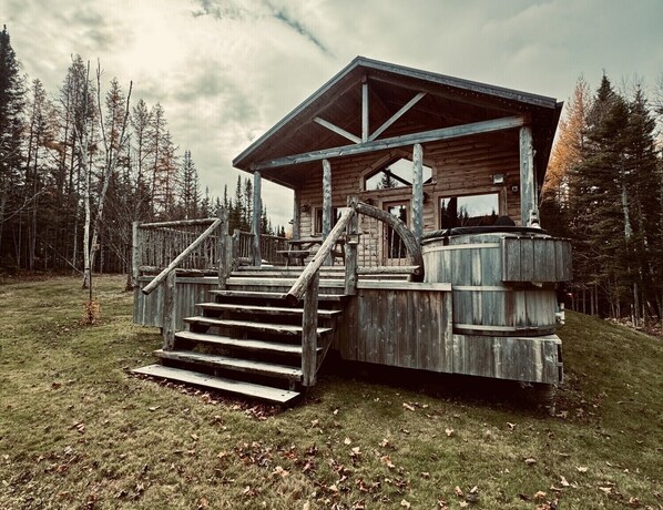 A rustic cabin with a wooden staircase leading to a porch, surrounded by trees.