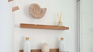 Casa de banho com estantes de madeira contendo produtos de higiene pessoal, uma concha decorativa e uma tomada.