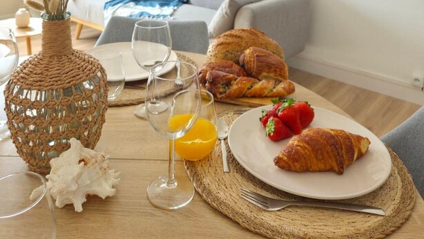 Uma área de refeições com uma mesa posta para o café da manhã, incluindo croissants, morangos e suco de laranja.