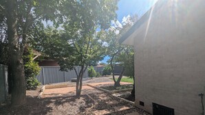 A courtyard with a paved walkway, trees, a brick wall, and a metal fence.