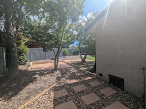Un patio con sendero empedrado, árboles, pared de ladrillo y cerca de metal.