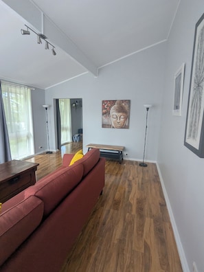 Een moderne woonkamer met een rode bank, houten vloeren en een Boeddha-schilderij aan de muur.
