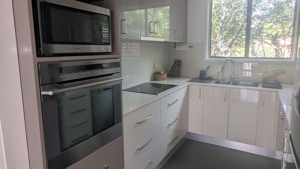 A modern kitchen with stainless steel appliances, white cabinetry, and a large window providing natural light.