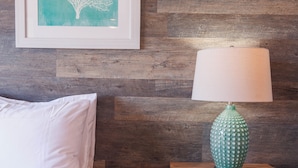 A neatly made bed with white bedding, a wooden nightstand with a green lamp, and a framed artwork on the wall. - Holo Hou Hale - Lahaina Shores Retreat on Front St (Lahaina)