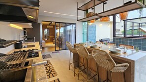 A modern kitchen with a gas stove, a dining area with wicker chairs, and a view through large windows. - Luxury penthouse apartment with air conditioning in all rooms in Ubatuba. (Ubatuba)