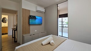 A hotel room with a bed, a TV mounted on the wall, a window with a view, and a door leading to a bathroom. - Luxury penthouse apartment with air conditioning in all rooms in Ubatuba. (Ubatuba)