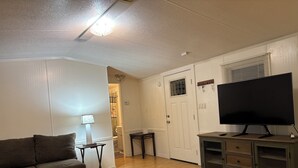 A living room with a sofa, a TV on a cabinet, a lamp, and a door leading to another room.
