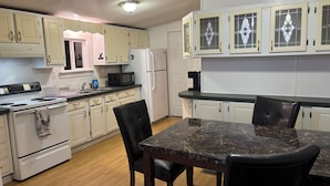 A kitchen with white cabinets, a black countertop, a stove, a refrigerator, and a dining table with chairs. - Farmhouse @ Grandma's place (Prairie Grove)