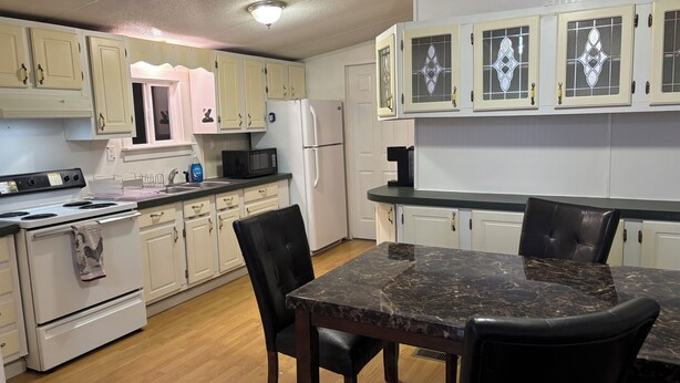 A kitchen with white cabinets, a black countertop, a stove, a refrigerator, and a dining table with chairs.