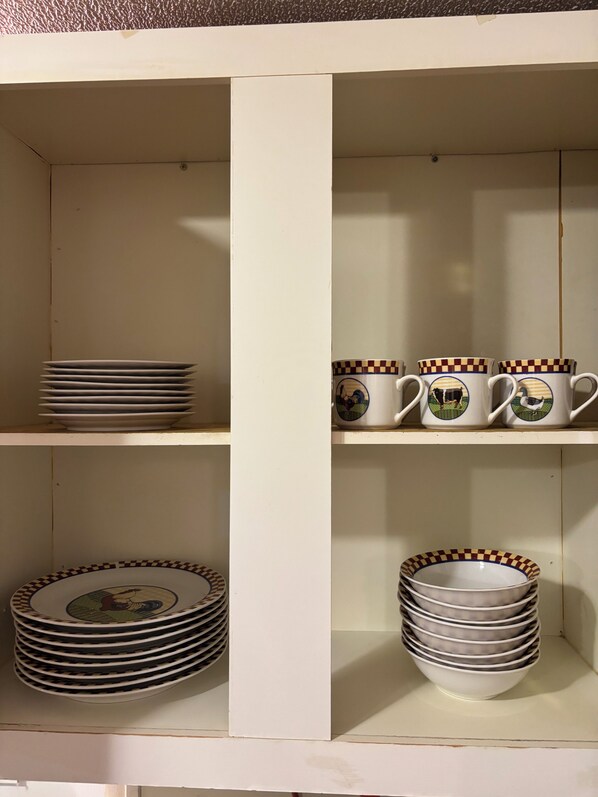 A white cabinet with shelves holding stacks of plates and bowls with checkered patterns.