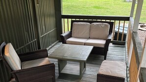A covered patio with wicker furniture, a table, and a view of a grassy yard.