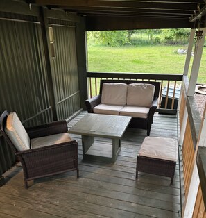 A covered patio with wicker furniture, a table, and a view of a grassy yard. - Farmhouse @ Grandma's place (Prairie Grove)