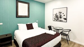Een keurig opgeruimde hotelkamer met een bed, nachtkastje en een eettafel met stoelen.