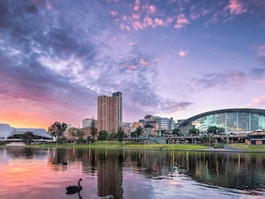 A cityscape with a large building, a modern structure, and a body of water reflecting the sky. - Private Ensuite City Stay (Adelaide)