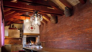 A rustic kitchen with a brick wall, wooden beams, a hanging chandelier, and a fireplace. - Three homes with pool and sauna in Gorski Kotar near Risnjak. (Crni Lug)