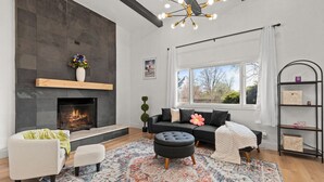 Ein modernes Wohnzimmer mit Kamin, einer Couch, einem Couchtisch und einem großen Fenster mit Blick auf Bäume.