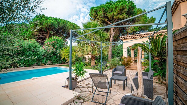 Ein Poolbereich mit einer Pergola, Gartenmöbeln und verschiedenen Pflanzen.