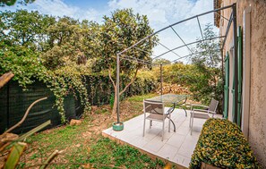 Een terras met een tafel en stoelen, omgeven door groen en een pergola.