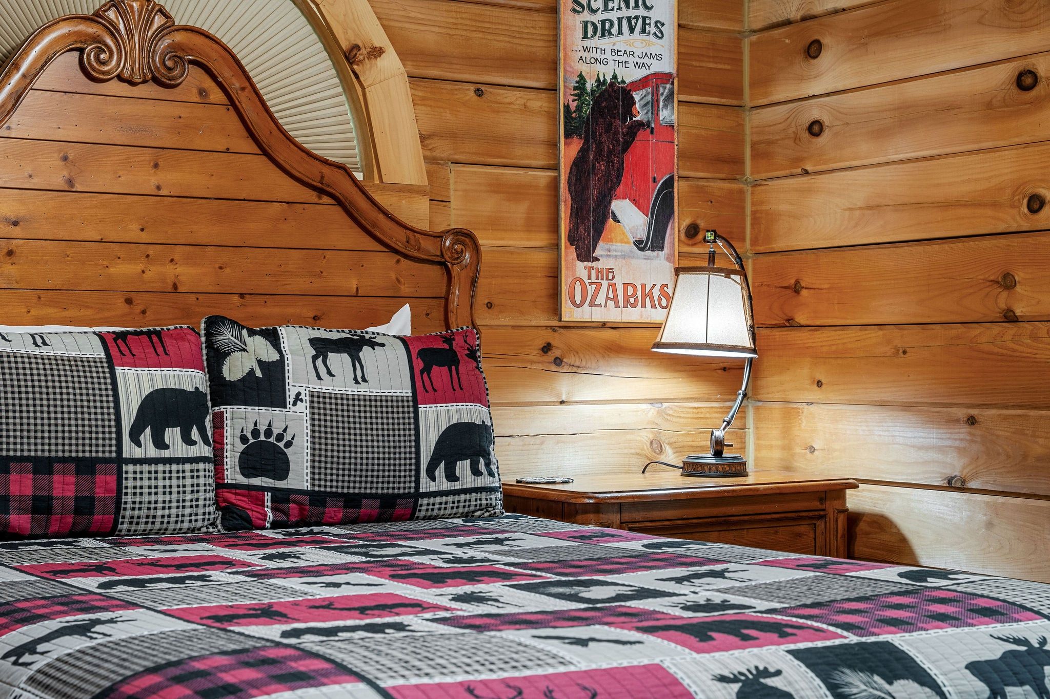 Een kamer met houten lambrisering, een bed met een quilt met dierenprint, een poster aan de muur en een bedlampje.