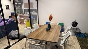 Ein Essbereich mit Holztisch und weißen Stühlen, eine Küche im Hintergrund und ein Grill im Freien.