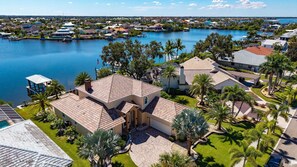 A residential area with houses near a body of water, featuring a large house with a patio and palm trees.
