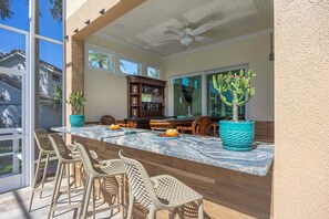 An outdoor patio with a marble countertop, bar stools, a ceiling fan, and potted plants.