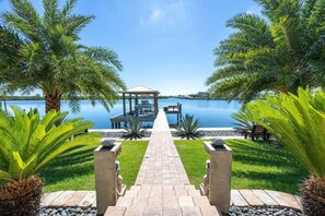 A pathway leading to a gazebo by a lake, surrounded by palm trees and a clear sky. - Private Beach & Pool Retreat, Dock, Kayaks & Dolphin Views - Seabird Shenanigans - Roelens (Apollo Beach)