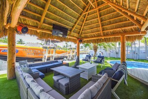 An outdoor lounge area with wicker furniture, a pool, and a thatched roof structure. - Captain's Cove | Canalfront w/ Pool & Boat Lift (Key West)