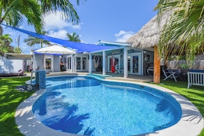A swimming pool with a blue border, a covered patio area, and a thatched-roof structure. - Captain's Cove | Canalfront w/ Pool & Boat Lift (Key West)