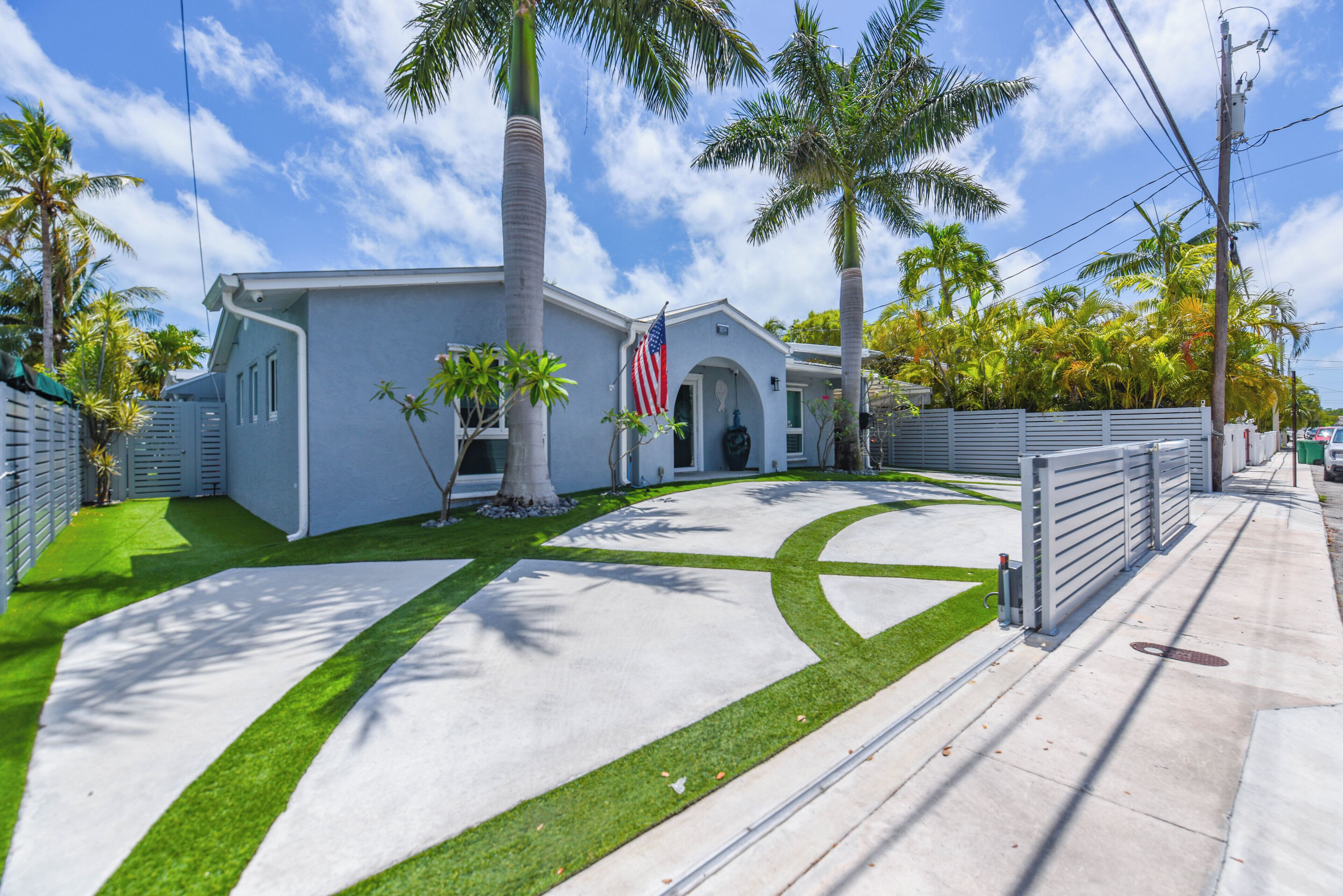 A house with a driveway, palm trees, and an American flag.