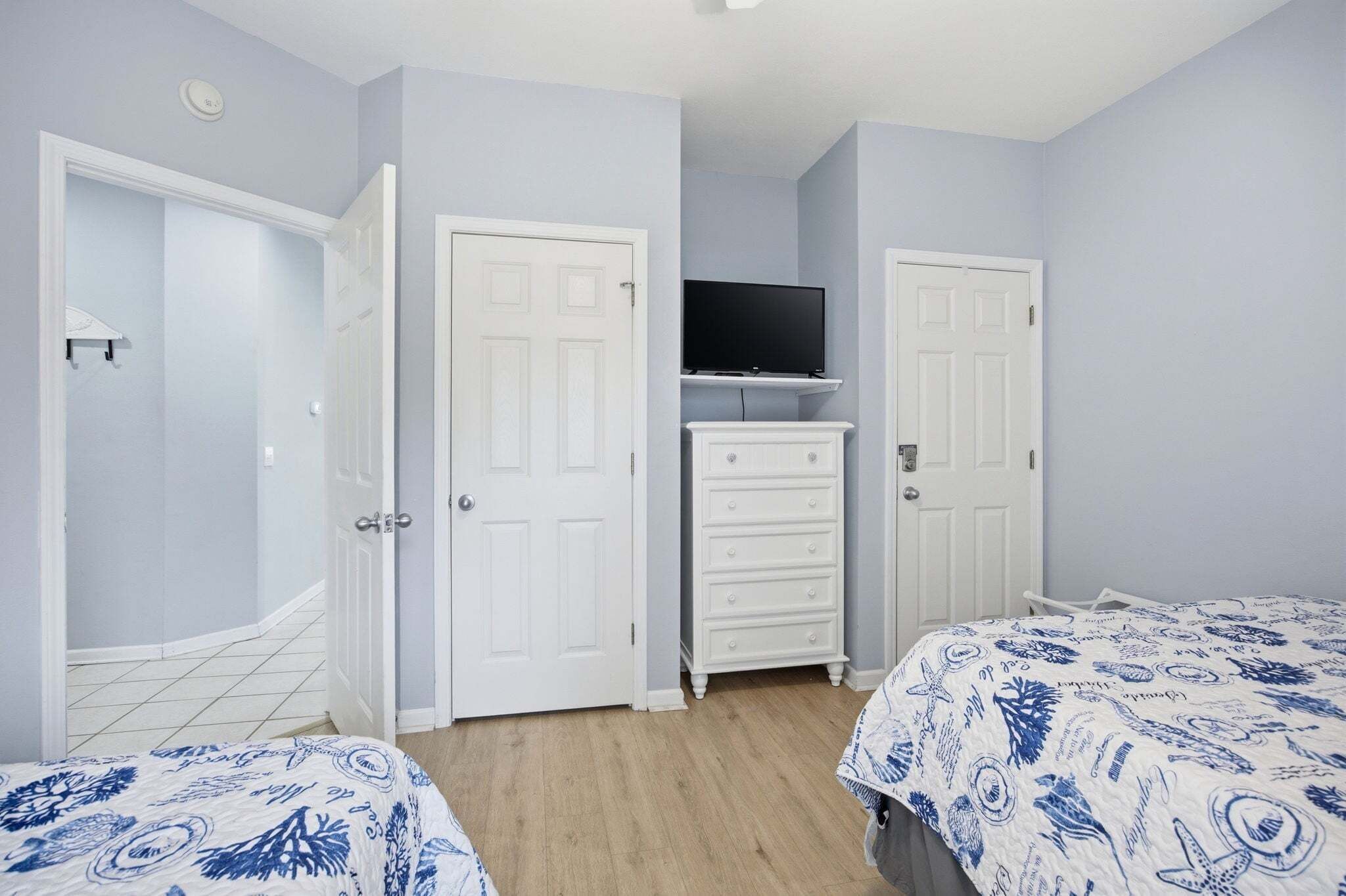 A bedroom with two beds, a dresser, a television on a stand, and two doors.