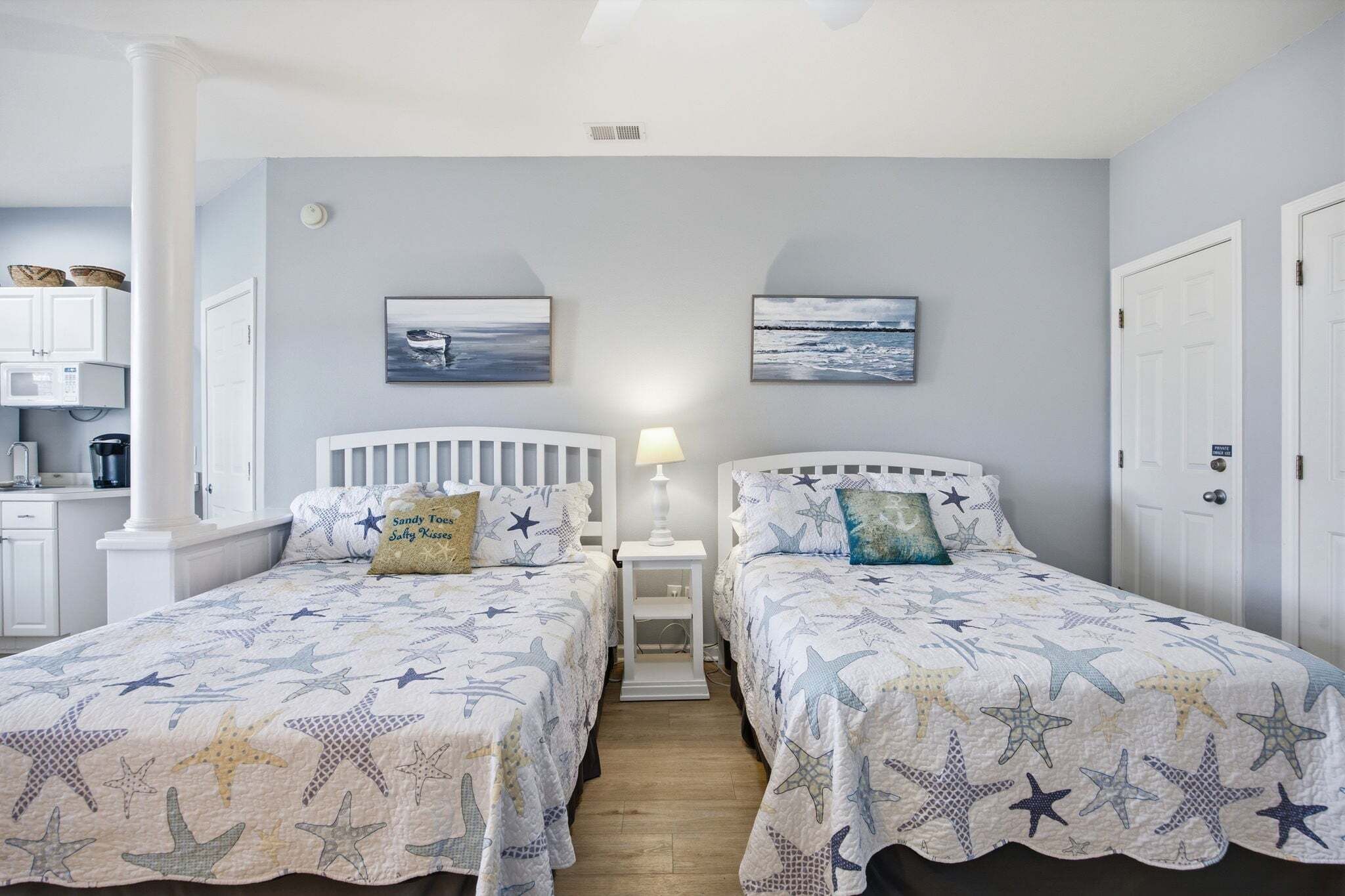 A bedroom with two beds, a nightstand, a lamp, and artwork on the wall.